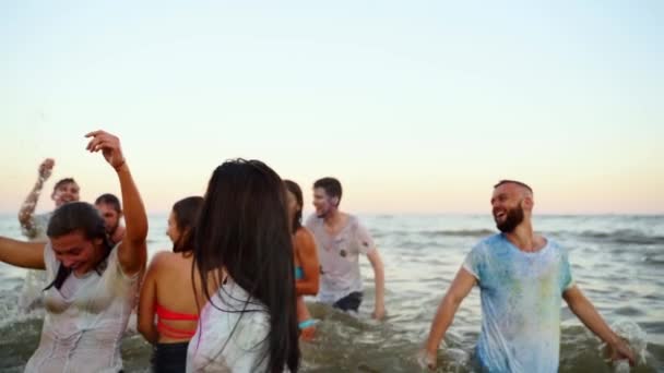 Pessoas alegres se divertem salpicando água no mar. Homens e mulheres de roupa e roupa de banho brincam no oceano. Os amigos celebram o festival Holi. Fim do bloqueio, isolamento pandémico vívido. Movimento lento. — Vídeo de Stock