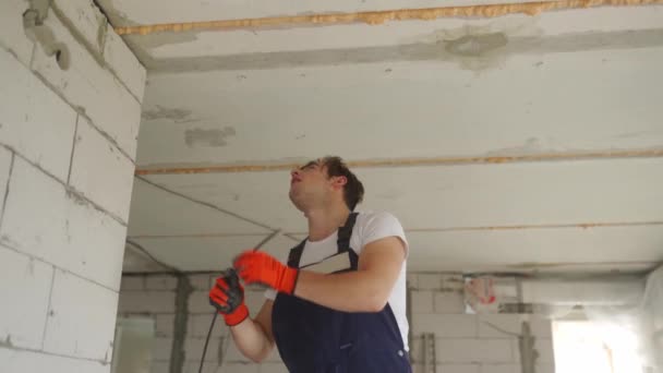 Electricista tendiendo cable de cableado, montando líneas eléctricas en la casa. Constructor en overoles y guantes instala cables eléctricos en el sitio de construcción. Hombre haciendo renovación de apartamentos. — Vídeos de Stock