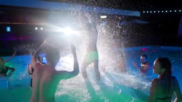 Друзья плескаются водой в бассейне для вечеринок. Веселая молодежь в купальниках веселится, танцует и веселится на роскошной курортной вилле. Счастливые мужчины и женщины тусуются. Медленное движение. — стоковое видео
