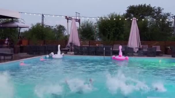 Gelukkige vrienden springen en spetteren in het zwembad in luxe resort. Jonge mannen in zwemkleding die 's nachts feesten in een privé vakantievilla. Jongens die in het water duiken. Langzame beweging. — Stockvideo