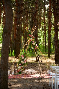 Pembe güllerle süslenmiş tahta çubuklardan yapılmış bohem çadır kemeri, halıdaki mumlar, pampass otları, çam ormanlarındaki açık hava düğün mekanında peri ışıklarına sarılmış. Çiçeksel kompozisyonlar.