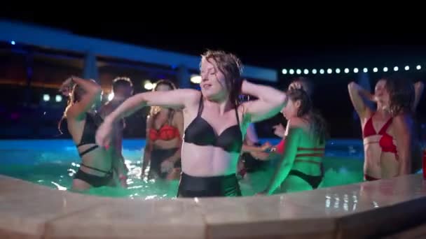 Mooie vrouw in bikini dansend en rondhangend met vrienden bij het nachtzwembadfeest. Mensen hebben plezier spetterend water en feesten met cocktails in luxe privé villa zwembad. Langzame beweging. — Stockvideo