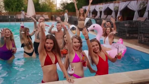 Hete meiden in bikini hebben een zwembadfeestje met cocktails in een luxe resort. Vrienden genieten van drankjes, rondhangen en uitgaan met opblaasbare praalwagens. Vrouwen ontspannen in het water. Langzame beweging. — Stockvideo