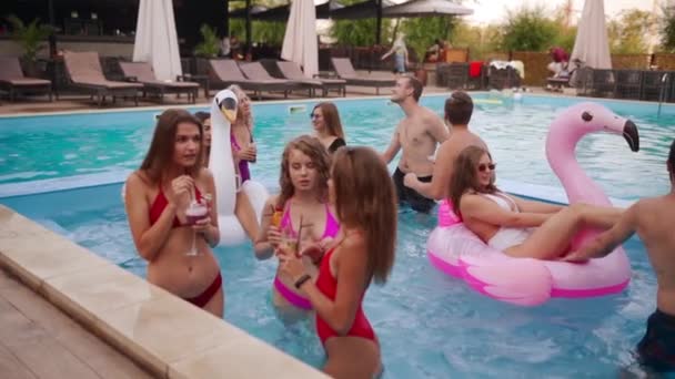People have swimming pool party with cocktails at a luxury resort. Friends in swimwear enjoying drinks, hanging out and clubbing with inflatable floats. Hot girls relax in the water. Slow motion. — Vídeo de stock