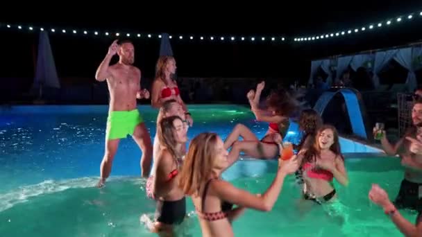 Vrienden hebben nachtzwembadfeest in een privé villa zwembad. Vrolijke jongeren in zwemkleding spetterend water, dansen en feesten in luxe resort. Gelukkige mannen en vrouwen die rondhangen. Langzame beweging. — Stockvideo