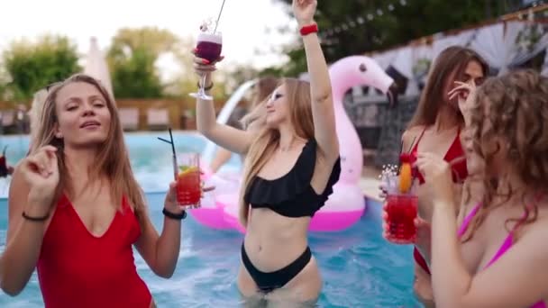Flickor i bikini har poolfest med cocktails i poolen. Kvinnor avkopplande klinkande glas med drycker på lyx resort. Kvinnliga vänner i röda badkläder dansar, klubbar i ett vatten. Långsamma rörelser. — Stockvideo