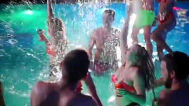 Gece havuzu partisinde yüzme havuzunda su sıçratan arkadaşlar. Mayo giyen, dans eden, lüks tatil köylerinde parti yapan neşeli gençler. Mutlu erkekler ve kadınlar birlikte takılıyor. Yavaş çekim.
