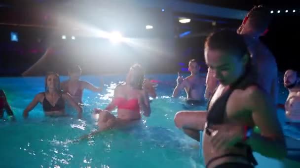 Gli amici organizzano una festa notturna in piscina in una villa privata. Giovani allegri in costume da bagno spruzzando acqua, ballando e festeggiando in resort di lusso. Uomini e donne felici che escono insieme. Rallentatore. — Video Stock