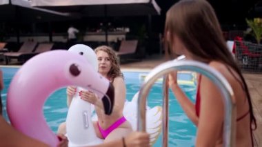 Havuzda yüzen bikinili seksi kızlar. Mayo giyen çekici, zayıf kadınlar şişme flamingoda, lüks otellerdeki havuz partisinde eğleniyorlar. Bayan arkadaşlar tatilde dinlenir..