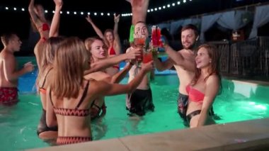 Bir grup arkadaş gece havuz partisinde kadeh tokuşturup kokteyl içiyorlar. Mayo giyen neşeli insanlar içki içer, dans eder, gece kulüplerine gider ve lüks tatil köylerinde parti yaparlar. Yavaş çekim.