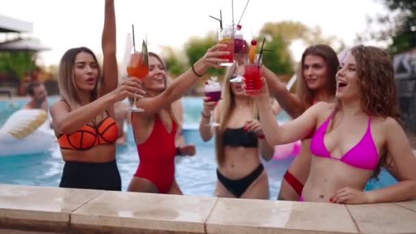 Dziewczyny w bikini mają imprezę przy basenie z koktajlami w basenie. Kobiety relaksujące kieliszki do drinków w luksusowym kurorcie. Przyjaciółki w czerwonych strojach kąpielowych tańczą w wodzie. Zwolniony ruch. — Wideo stockowe