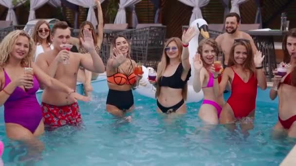 People have swimming pool party with cocktails at luxury resort. Friends in swimwear clinking glasses with drinks, dancing, cheering, clubbing with inflatable floats. Hot girls in water. Slow motion — Stockvideo