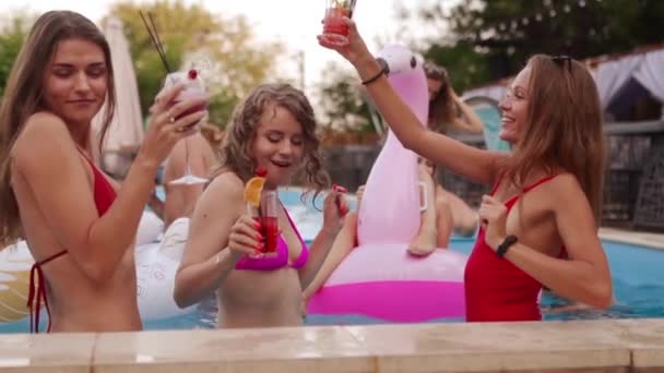 Filles chaudes en bikini ont piscine partie avec des cocktails dans un complexe de luxe. Amis dégustant des boissons, traînant et clubbing avec flotteurs gonflables. Les femmes se détendent dans l'eau. Mouvement lent. — Video