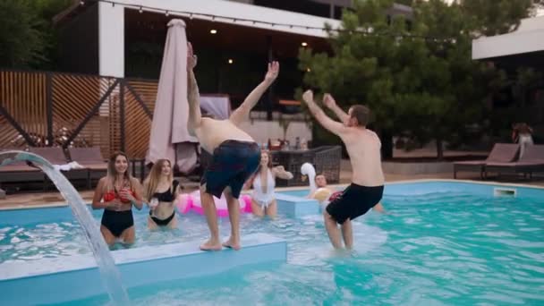 Friends have pool party dancing in private villa swimming pool. Cheerful young people in swimwear jump and dive splashing water in luxury resort. Men and women hanging out in slow motion. — Vídeo de Stock