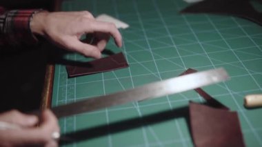 Yakın plan eller bıçakla deri desenleri oyar ve fazlalık kısımları çıkartır. Tanner, terzi tezgahın arkasında çalışıyor ve deri eşyalar yapıyor. El yapımı..