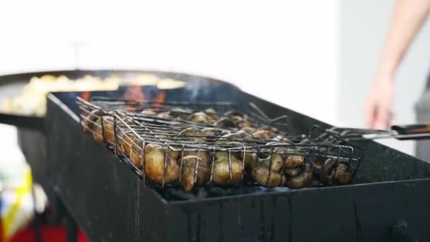 Close-up of chef frying mushrooms on skewers on a large industrial stove grill outdoors for a catering food service. The cook turns spits on bbq. — ストック動画