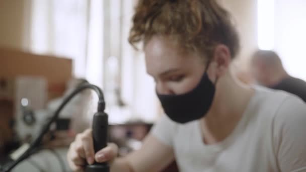 Trabajadora del centro de servicio de reparación electrónica femenina repara tableros de computadoras y microchip de soldadura con pistola de calor. Mujeres con máscara. Ocupaciones técnicas. Chica mirando a la cámara. — Vídeos de Stock