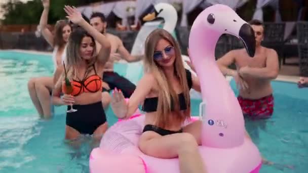 Mooie vrouw in bikini badpak opknoping out op opblaasbare roze flamingo matras op nacht zwembad partij. Vrienden feesten met cocktails in vakantievilla. — Stockvideo