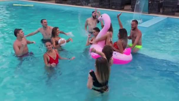 Amigos tienen fiesta en la piscina nocturna en una piscina villa privada. Jóvenes felices en traje de baño salpicando agua, bailando con flotadores y colchón inflable en resort de lujo. — Vídeos de Stock