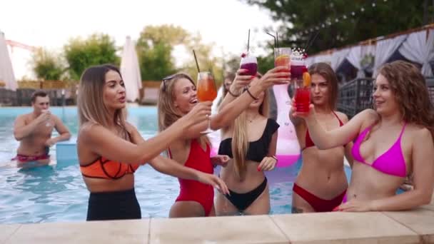 Las chicas en bikini tienen fiesta en la piscina con cócteles en la piscina. Mujer relajante tintineo vasos con bebidas en el complejo de lujo. Amigas en traje de baño rojo bailando, bailando en el agua. Movimiento lento. — Vídeos de Stock