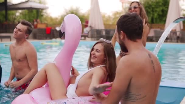 Een meisje in bikini met een vriendje op een zwembadfeest. Paar kusjes die plezier hebben op opblaasbare roze flamingo float matras. Liefhebbers feesten en dansen in zwemkleding op huwelijksreis tropische vakantie. — Stockvideo
