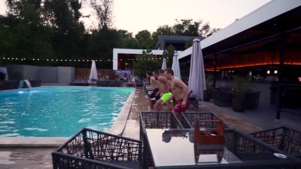 Щасливі друзі стрибають у басейн у розкішному курортному готелі. Молоді чоловіки в купальнику проводять вечірку в приватній віллі. Хлопці занурюються у воду. Повільний рух . — стокове відео