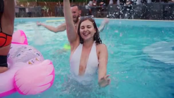 Friends have night pool party in a private villa swimming pool. Happy young people in swimwear splashing water, dancing with floaties and inflatable mattress in luxury resort. Slow motion. — Vídeo de Stock