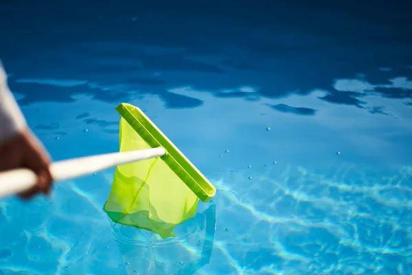 Hombre con equipo de red skimmer limpieza piscina de la basura. Servicio y mantenimiento de la piscina. El macho elimina la basura del agua con una savia. Servicio de limpieza de piscinas. Limpiador hotel. — Foto de Stock