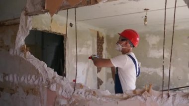 Müteahhit balyozla duvarı yıkar ve yeniden düzenleme için delik açar. Adam elle sökme ve yıkım işleriyle uğraşıyor. Dairenin tadilatı için büyük çekiçle vuruyor. Üniformalı inşaat işçisi.