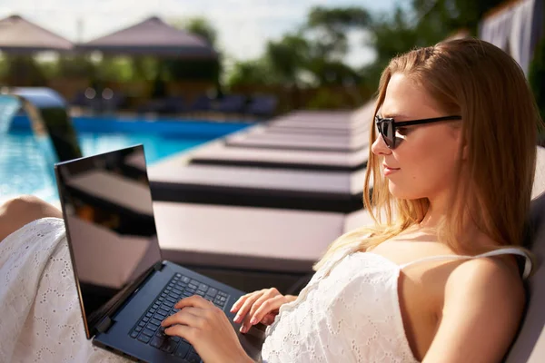 Self employed woman telecommuting with team on project from tropical island resort. Freelancer businesswoman doing remote work with laptop on swimming pool beach bed at spa. Girl tanning and relaxing. — Fotografia de Stock