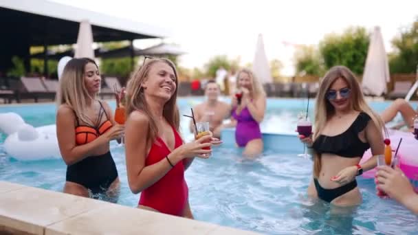 Girls in bikini have pool party with cocktails in swimming pool. Women relaxing clinking glasses with drinks at luxury resort. Female friends in red swimwear dancing, clubbing in a water. Slow motion. — Wideo stockowe