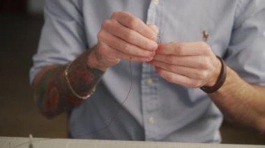 Deri ustası atölyesinde çalışıyor. Usta deri cüzdan yapıyor. Atölyede iğne ve iplikle dikiş malzemeleri ve aksesuarları olan bir adam..