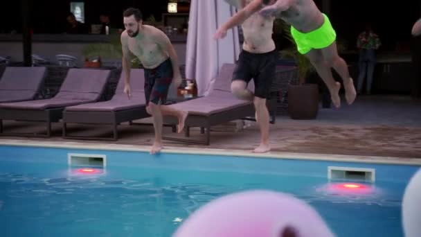 Щасливі друзі стрибають у басейн у розкішному курортному готелі. Молоді чоловіки в купальнику проводять вечірку в приватній віллі. Хлопці занурюються у воду. Повільний рух . — стокове відео