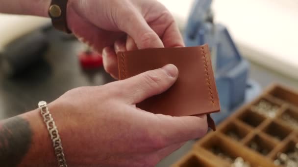 Leather craftsman works in workshop. Master making leather wallet. Man installs tack button snap fastener fitting using hand press grommet machine. Male using manual punch tool for fastener sewing. — Stock Video