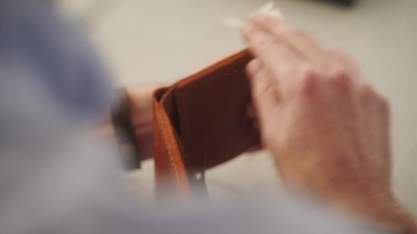 Artesano de cuero trabaja en su taller. Maestro haciendo una billetera de cuero bifold con bolsillo de moneda y titular de la tarjeta. El hombre pule y termina un producto. — Vídeo de stock