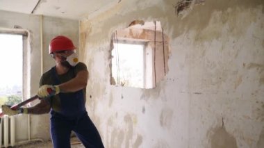 Müteahhit balyozla duvarı yıkar ve yeniden düzenleme için delik açar. Adam elle sökme ve yıkım işleriyle uğraşıyor. Dairenin tadilatı için büyük çekiçle vuruyor. Yavaş çekim.