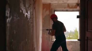 Döner çekiç matkabıyla çalışan bir inşaatçı. Müteahhit, apartman tadilatı ve yenileme için duvarı delmek üzere beton matkapla delik açıyor. Üniformalı elektrikçi elektrik tesisatı kuruyor.