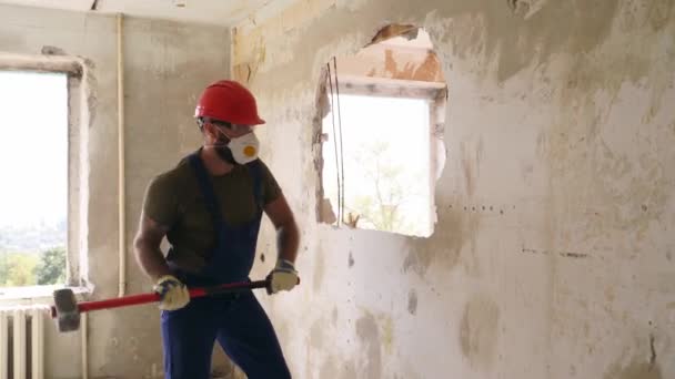 Contractor wrecks wall with sledgehammer making hole for rearrangement. Man doing manual dismantling and demolition works with big hammer hits for apartment renovation. Construction worker in uniform. — Stock Video