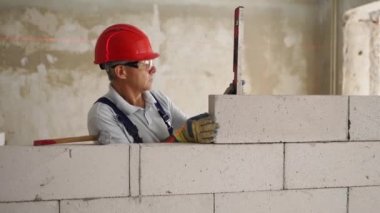 Duvardaki beton blokları kontrol etmek için ruh balonu ve lazer seviyesini kullanıyor. Müteahhit tuğla işi için aletler kullanır. İşçi yeni apartman dairesine duvar örüyor..