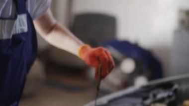 Kadın tamirci motor yağı seviyesini inceliyor. Tulumlu ve koruyucu eldivenli kadın araba tamir servisindeki motor ve parçaları kontrol ediyor. Modern atölyede araç tamiri hatası.