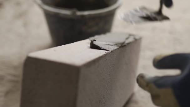 A téglalap ragasztó ragasztót alkalmaz az autoklávozott szénsavas betontömbökre, fogazott vakolattal és spatulával. A kőműves kivitelező habarcsot rak a habból készült betonra, és kőművesmunkát végez az építkezésen.. — Stock videók
