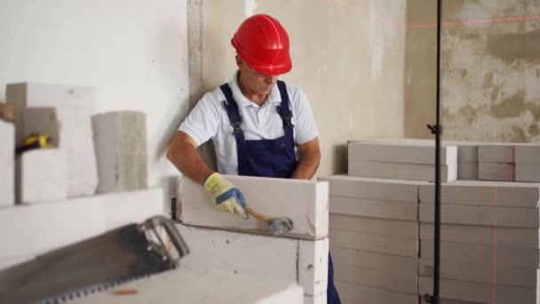 Murbruk med hjälp av gummiklubba för att knacka och jämna betongblock vägg. Entreprenören använder exakt sprit bubbla och laser nivå för tegel. Arbetstagare bygger en vägg i ny lägenhet fastigheter. — Stockvideo