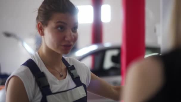 Lavoratrice meccanica in autoservice parla di riparato auto al cliente in officina e riportando i dettagli del lavoro, dà consigli. Donna forte, professioni professionali tema. — Video Stock