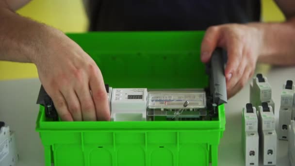 Electricien assemble la boîte de fusible de panneau électrique dans l'atelier. Travailleur installe compteur d'énergie, interrupteurs et disjoncteurs dans le tableau de distribution sur la table. — Video