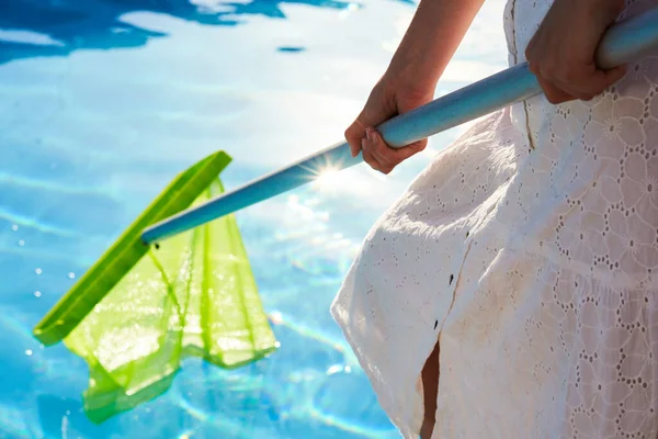 Mulher com equipamento de rede skimmer limpeza piscina de lixo. menina remove o lixo da água com uma seiva. Serviço de limpeza e manutenção de piscinas. Hotel limpador. — Fotografia de Stock