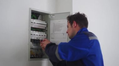 Elektrikçi elektrik sigorta kutusunu söker. Üniformalı usta elektrik panelinin vidalarını tornavidayla söküp elektriği tamir ediyor. Tamirci şalter ve şalterleri tamir ediyor..
