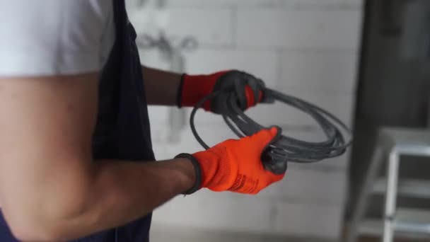 Electricista tendiendo cable de cableado, montando líneas eléctricas en la casa. Constructor en overoles y guantes instala cables eléctricos en el sitio de construcción. Hombre haciendo renovación de apartamentos. — Vídeos de Stock