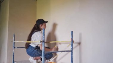 Kadın ressam, inşaat alanındaki iskeleye tekerlekli sandalyeyle duvar boyuyor. Tulumlu genç bir kadın ev dekorasyonu yapıyor, sahne dekorasyonu yapıyor. Profesyonel işçi odada DIY onarımı yapıyor..