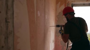 Döner çekiç matkabıyla çalışan bir inşaatçı. Müteahhit, apartman tadilatı ve yenileme için duvarı delmek üzere beton matkapla delik açıyor. Üniformalı elektrikçi elektrik tesisatı kuruyor.