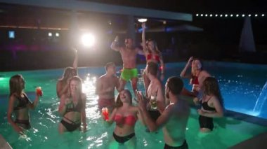 Arkadaşların özel villa havuzunda gece havuzu partisi var. Mayo giymiş neşeli genç insanlar su sıçratıyor, dans ediyor ve lüks otellerde parti yapıyorlar. Mutlu erkekler ve kadınlar birlikte takılıyor. Yavaş çekim.